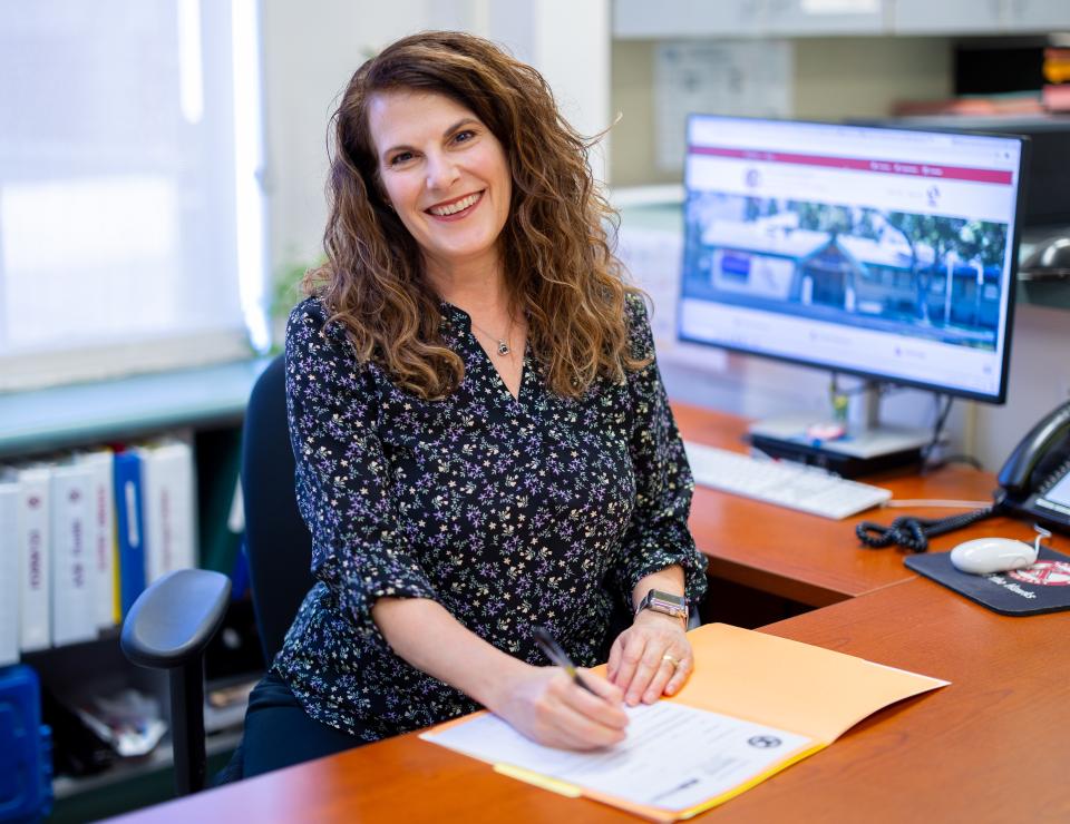 Administrative staff sitting at desk in front of an open folder, smiling and holding a pen.